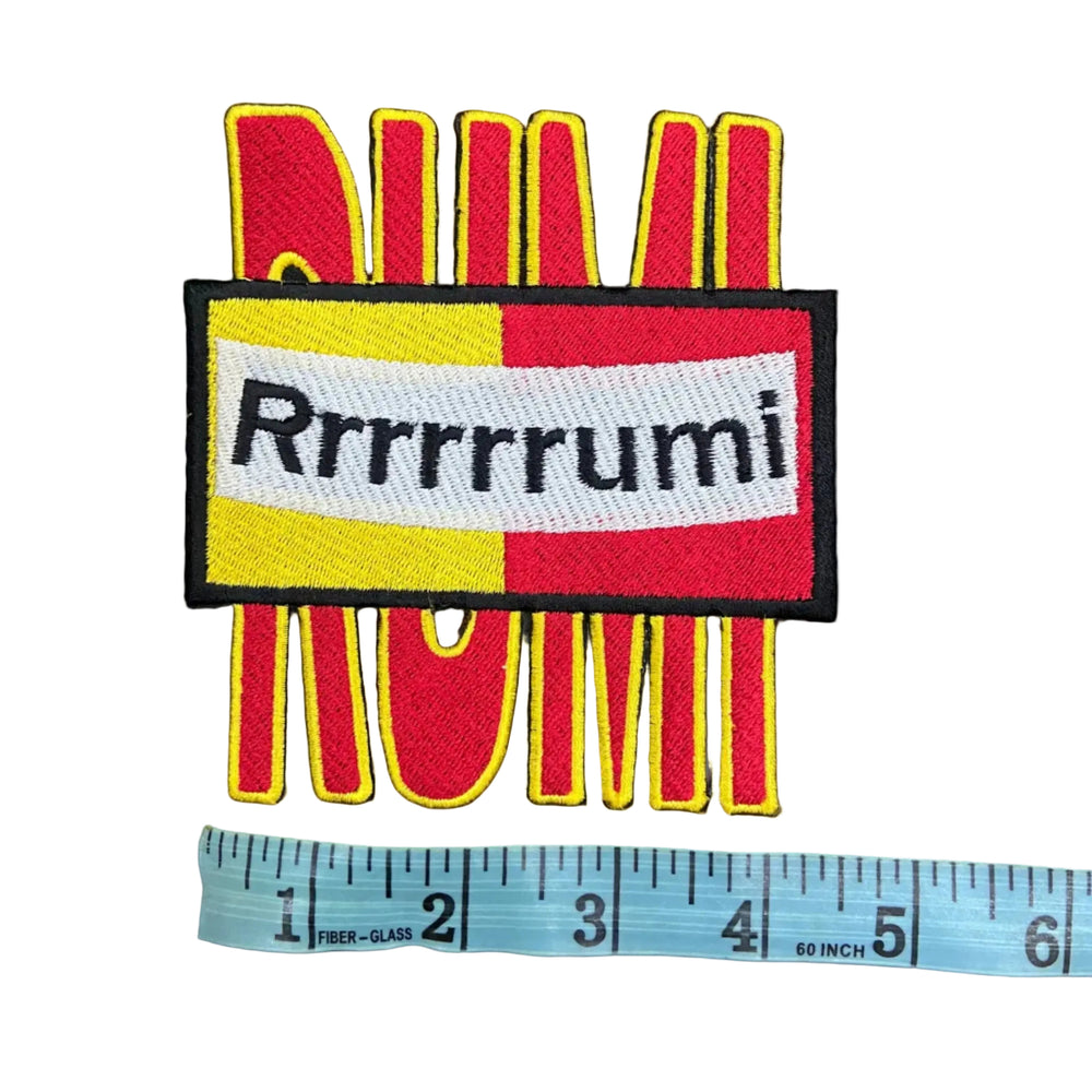 Colorful patch with 'Rrrrrumi' text and a ruler for scale on a dark background
