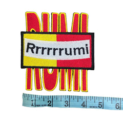 Colorful patch with 'Rrrrrumi' text and a ruler for scale on a dark background