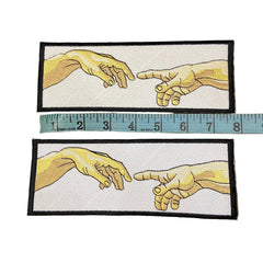 Two embroidered patches of hands with a ruler for scale on a dark background