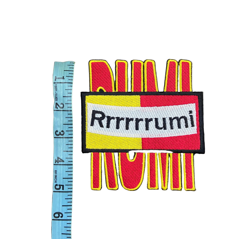 Colorful patch with text and design, measured against a ruler on a gray background