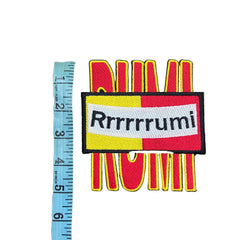Colorful patch with text and design, measured against a ruler on a gray background