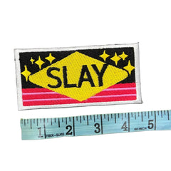 Embroidered patch with 'SLAY' text and stars on a gray background, next to a ruler for scale.