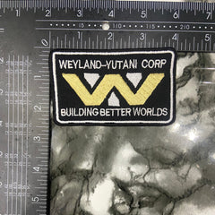 Patch with 'Weyland -Yutani Corp' logo on a textured surface with a ruler for scale.