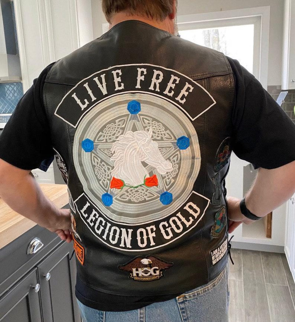 Person wearing a black leather vest with 'Live Free Legion of Gold' design in a custom patch.