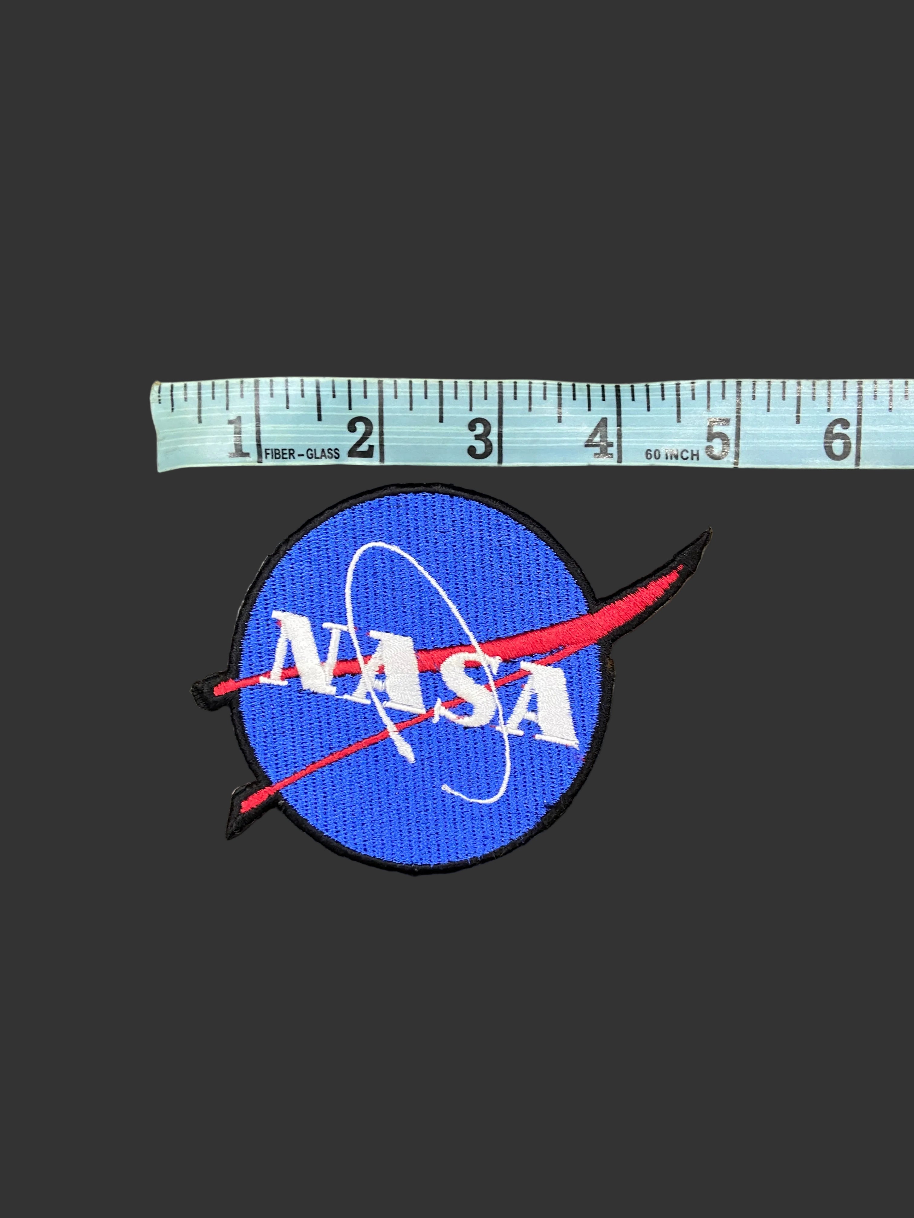 NASA patch with a ruler for scale on a gray background