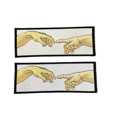 Two embroidered patches with hands reaching towards each other on a dark background