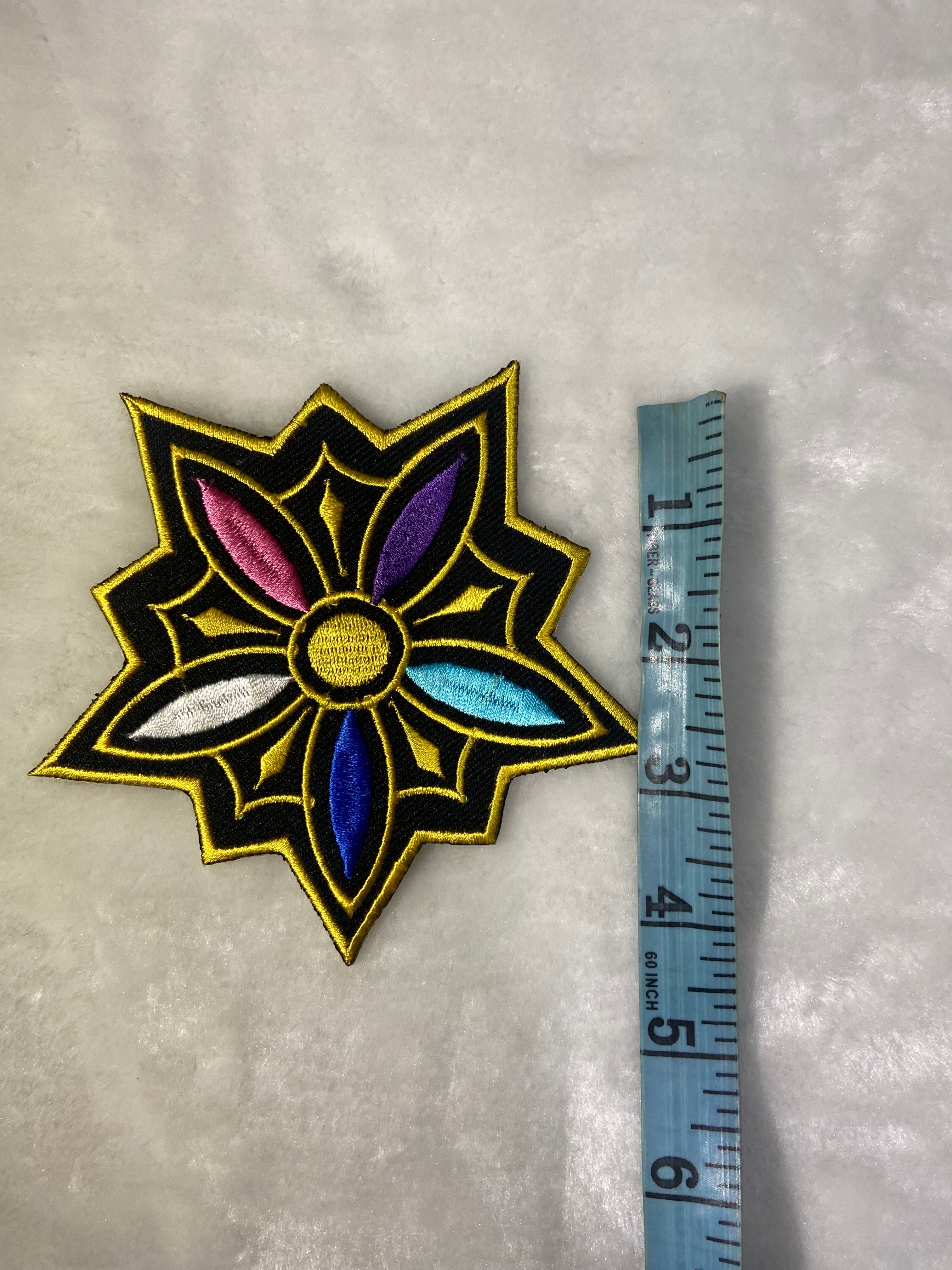 Decorative patch with a star-like design on a textured surface, measured against a ruler.