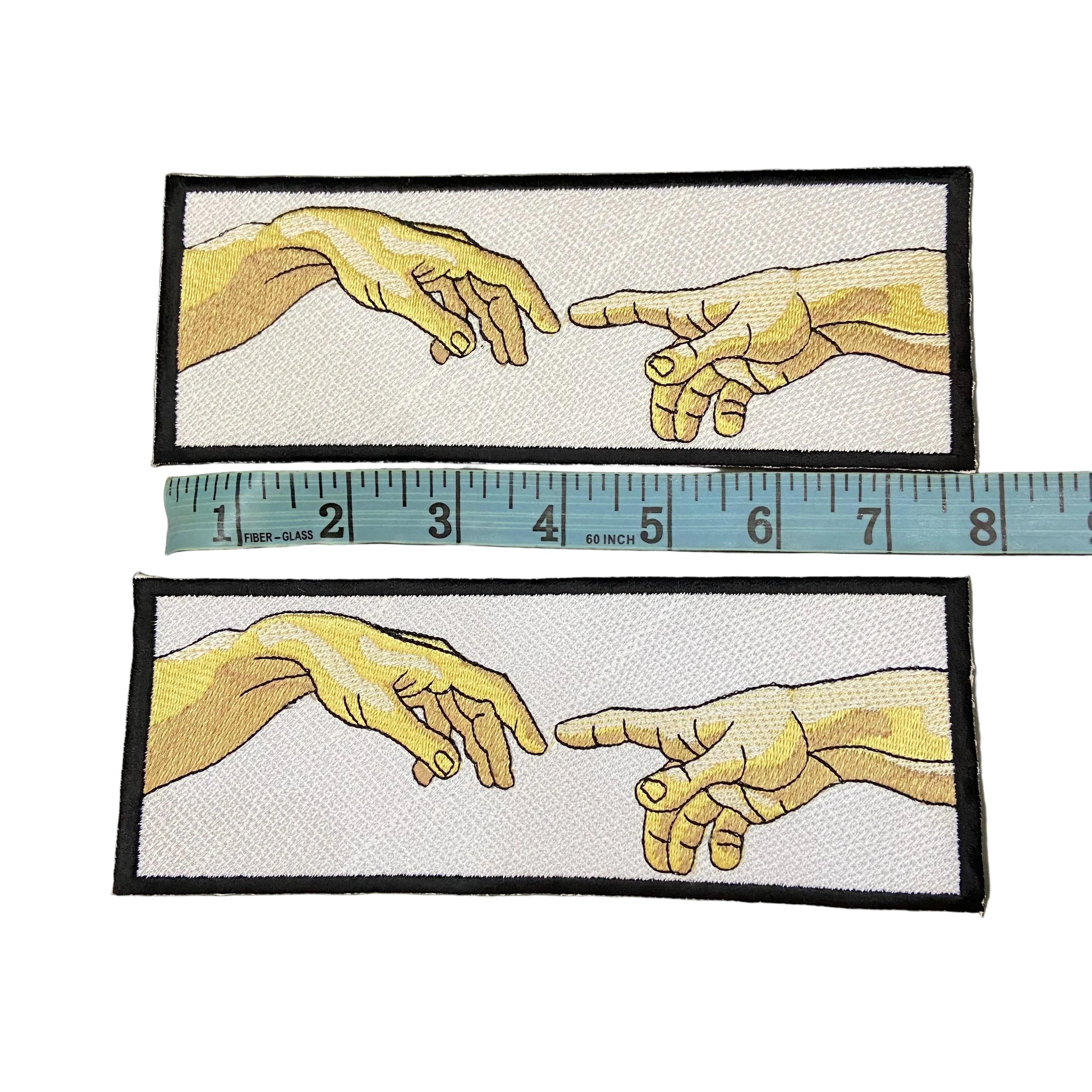 Two embroidered patches of hands with a ruler for scale on a dark background