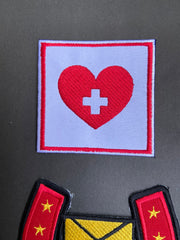 Patch with red heart and white cross on light background, next to another patch with yellow stars on a dark gray background.