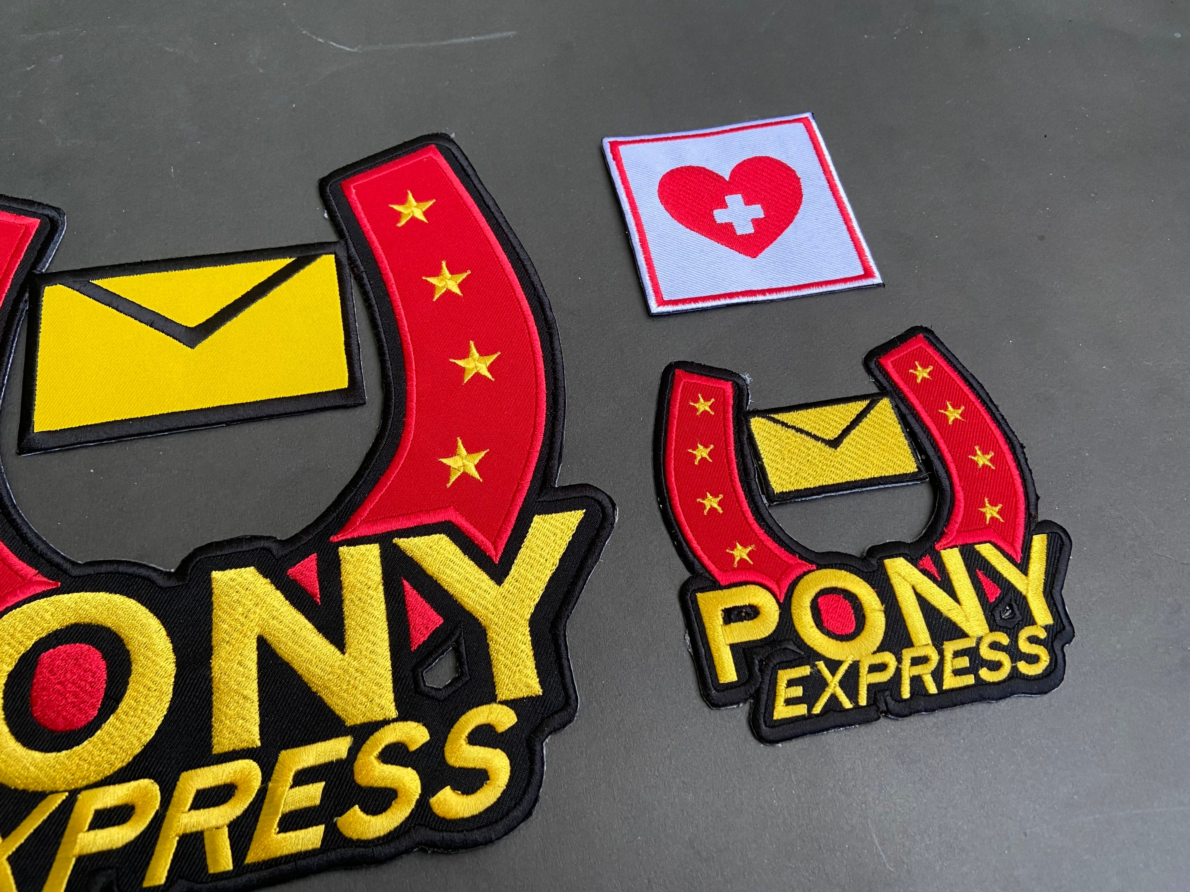 Pony Express patches with a heart and cross patch on a dark background