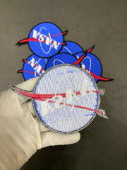 Embroidered patch with a design on a gloved hand, with additional patches in the background.