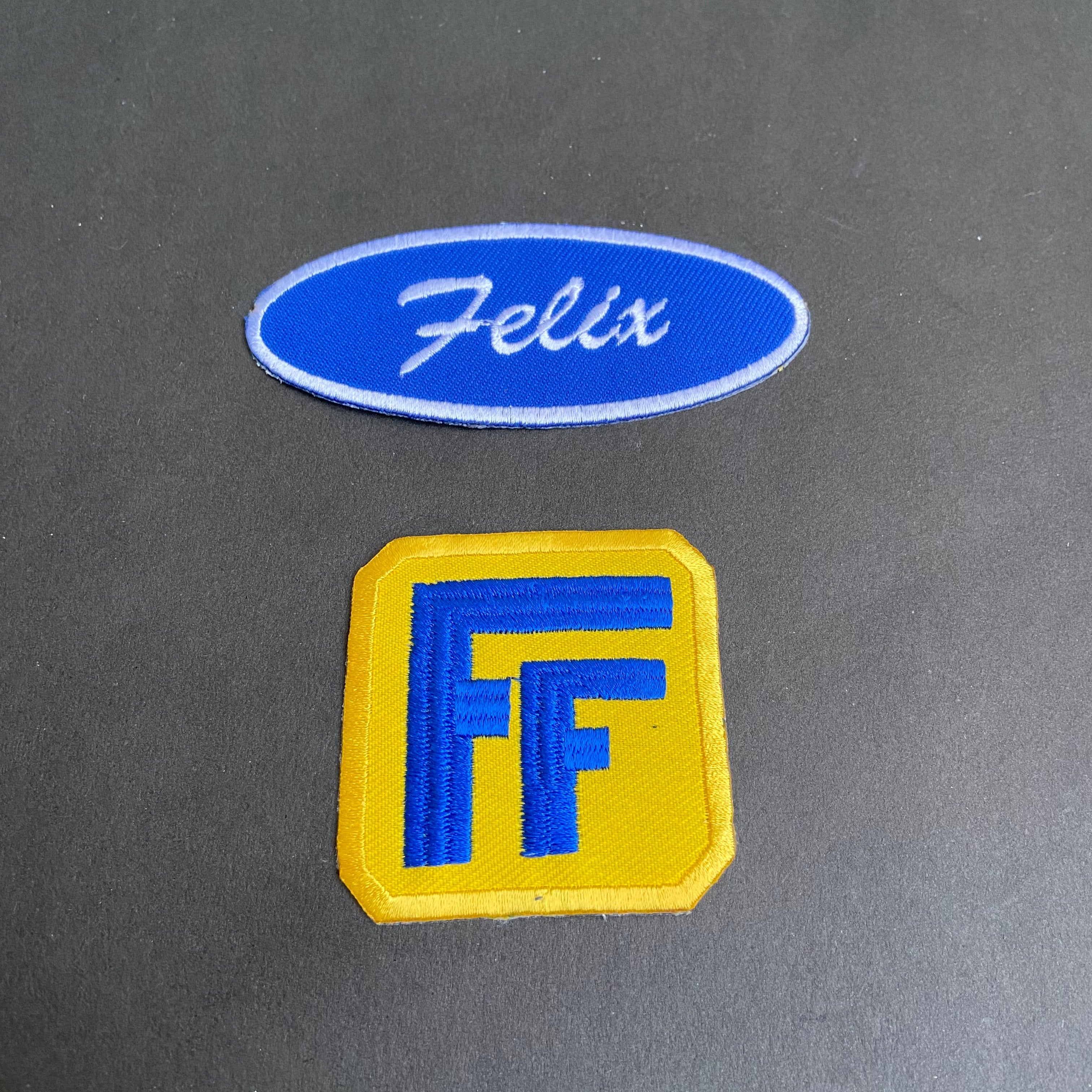Two patches, one blue and one yellow with a logo, on a dark gray background.