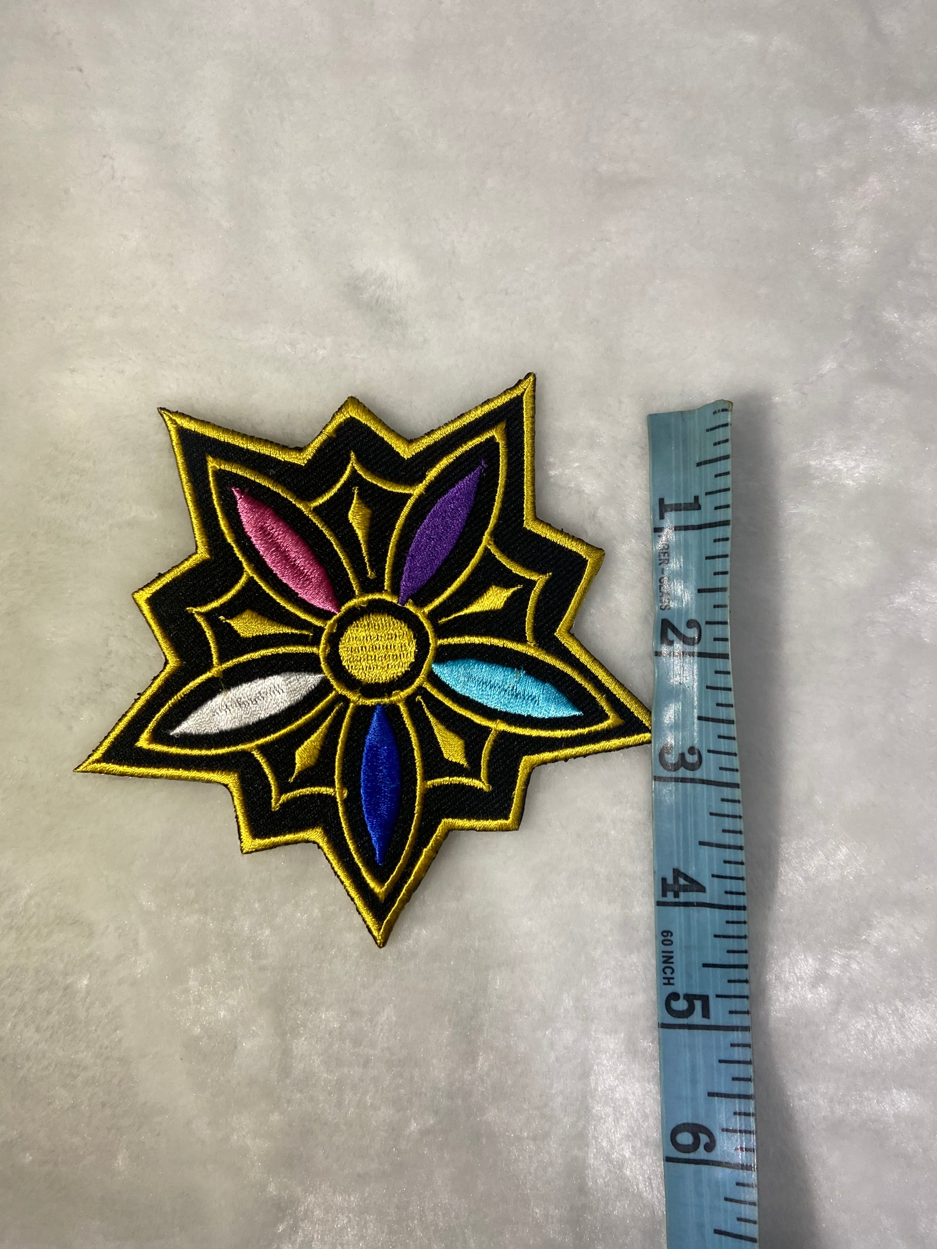 Decorative patch with a star-like design and colorful center, measured against a ruler on a gray background.