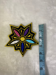 Decorative patch with a star-like design and colorful center, measured against a ruler on a gray background.