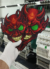 cyberpunk devil illuminati patches. red illuminati symbols

A hand wearing a white glove holds up a large embroidered patch featuring two red devil faces with glowing green eyes and yellow teeth, with an industrial embroidery machine in the background.